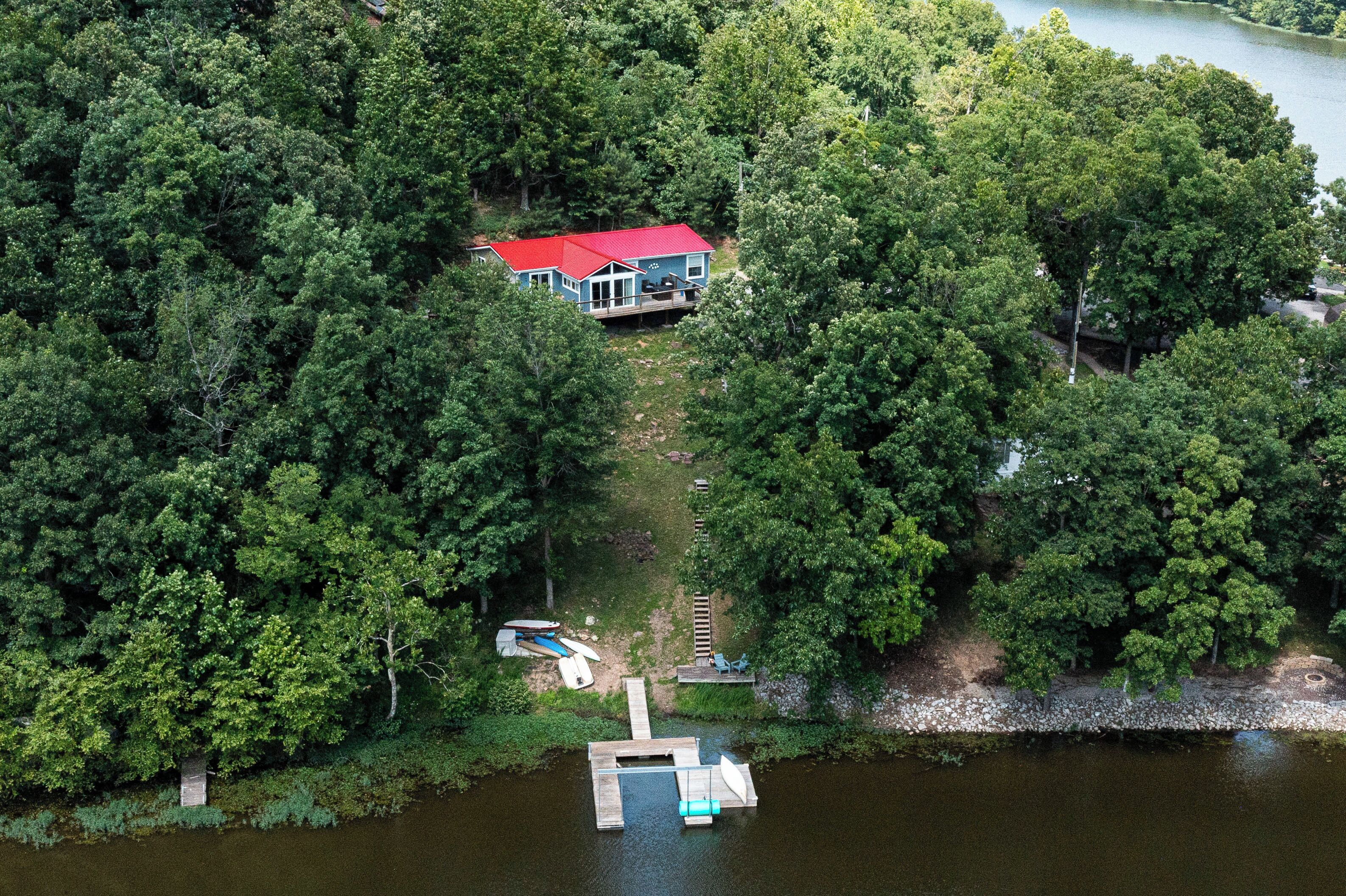 A house surrounded by dense forest, a dock, and a small boat.