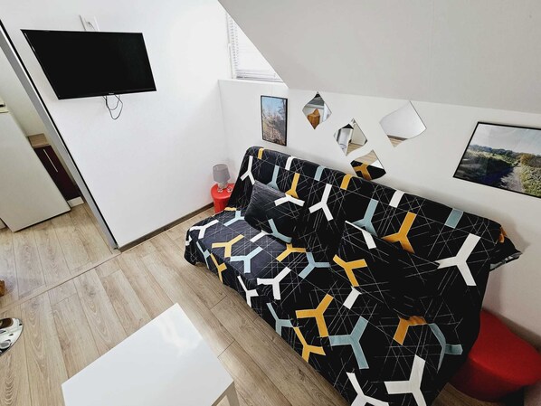 Una sala moderna con un sofá estampado en blanco y negro, un televisor de pantalla plana montado en la pared y una mesita de noche con una lámpara.