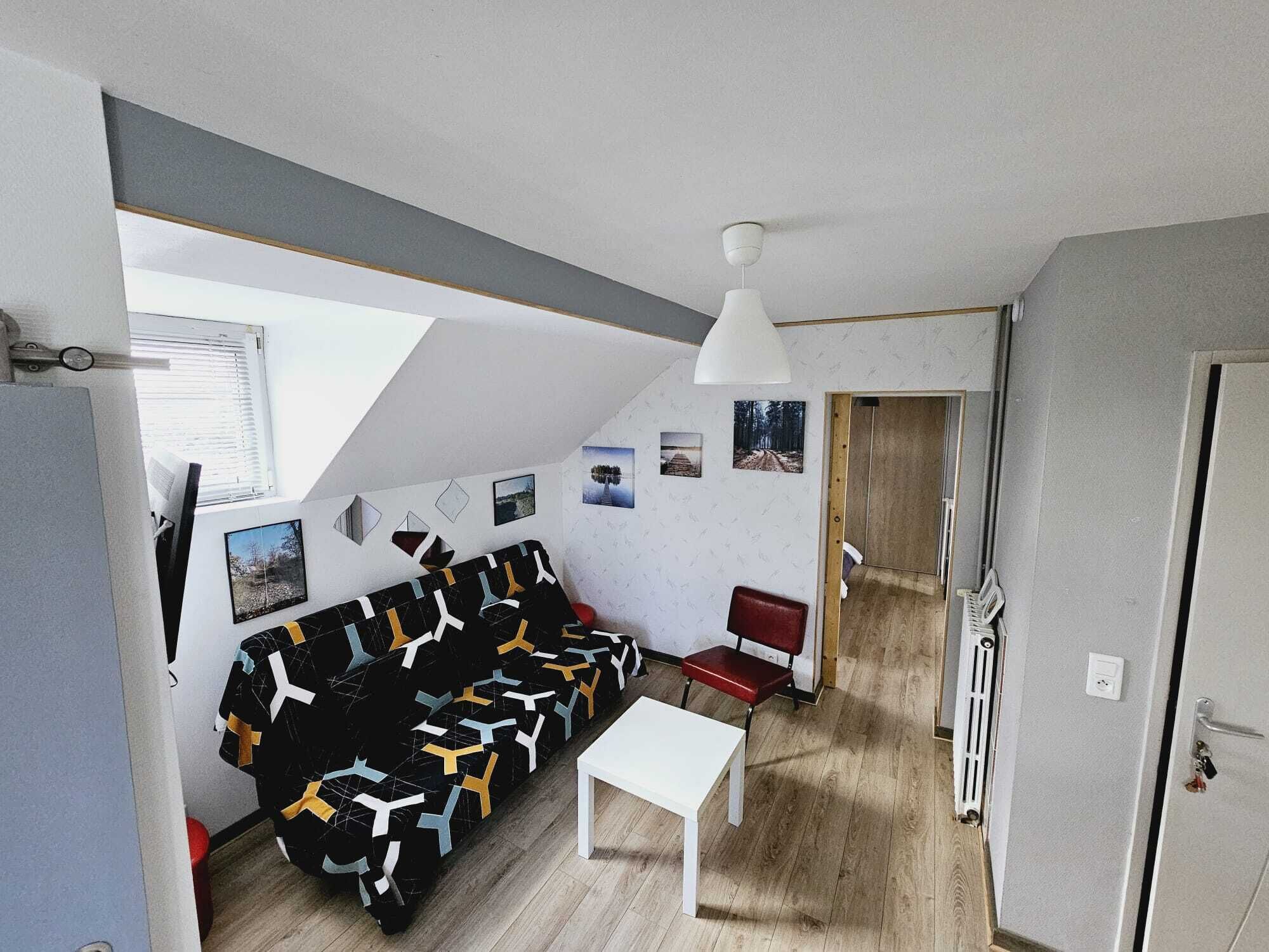 Un espacio habitable compacto con techo inclinado, un sofá de estampado geométrico, una mesa blanca y una silla roja.