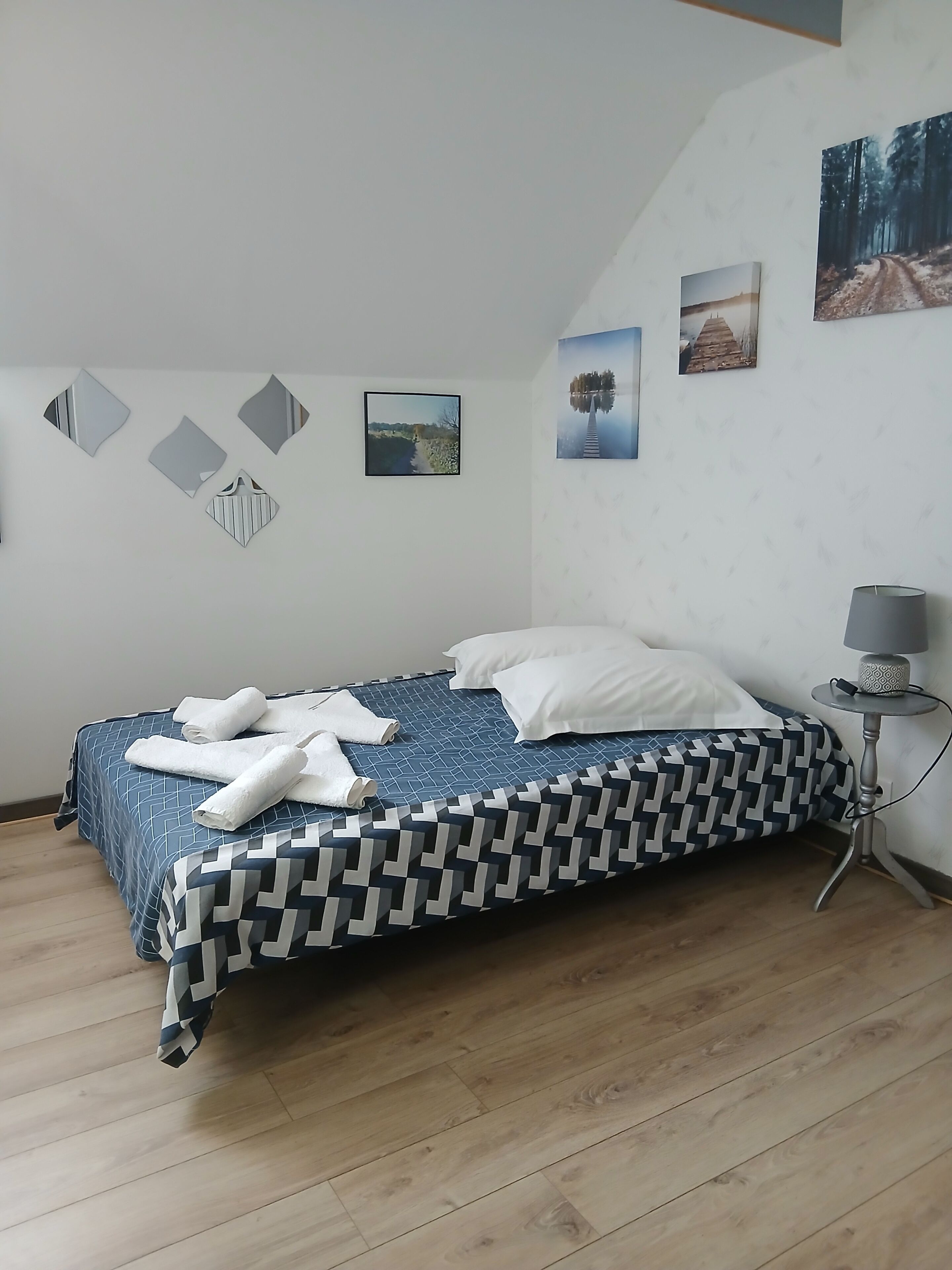 A bedroom with a bed, a bedside table with a lamp, and wall art.