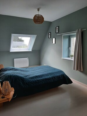 Une chambre à coucher avec un grand lit, une lucarne, une fenêtre avec des rideaux et une table de chevet avec une lampe.