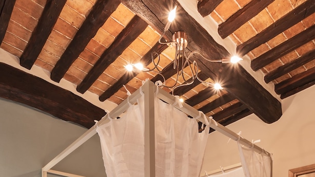 Ein Schlafzimmer mit Himmelbett, Holzbalken an der Decke und einem Nachttisch mit Lampe.