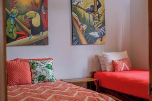 A hotel room with two beds, each with red bedding and patterned pillows. There are two paintings on the wall depicting tropical wildlife.