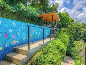 A staircase leading to a wooden deck with a railing, surrounded by lush greenery.