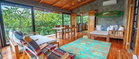 A spacious room with a wooden ceiling, a dining area, and a view of lush greenery.