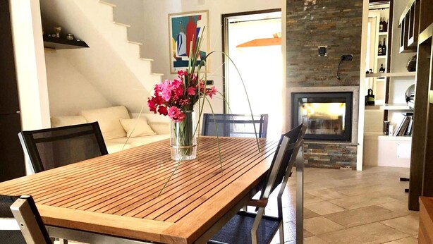 A dining area with a wooden table and chairs, a vase with flowers, a staircase, and a fireplace. - Graziosa Casetta nel Cuore di Porto Ottiolu (Porto Ottiolu)