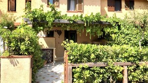 A building with a tiled entrance, a covered porch with vines, and a garden area with various plants. - Graziosa Casetta nel Cuore di Porto Ottiolu (Porto Ottiolu)