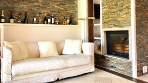 A living room with a white sofa, a fireplace, and a wall with a mosaic of variously colored tiles. - Graziosa Casetta nel Cuore di Porto Ottiolu (Porto Ottiolu)