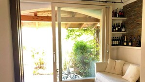 A modern living room with a sliding glass door leading to a patio, a white sofa, and a wine rack with bottles. - Graziosa Casetta nel Cuore di Porto Ottiolu (Porto Ottiolu)