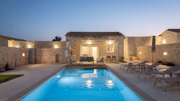 A swimming pool with lounge chairs and a patio area with stone walls and outdoor furniture. - Evaero Villa II, Family Retreat with a 32m² Pool (Prinos)