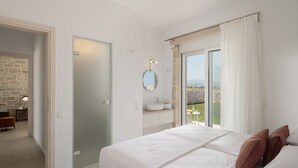 A bedroom with a large bed, a bathroom with a round mirror, and a view of the outdoors. - Evaero Villa II, Family Retreat with a 32m² Pool (Prinos)