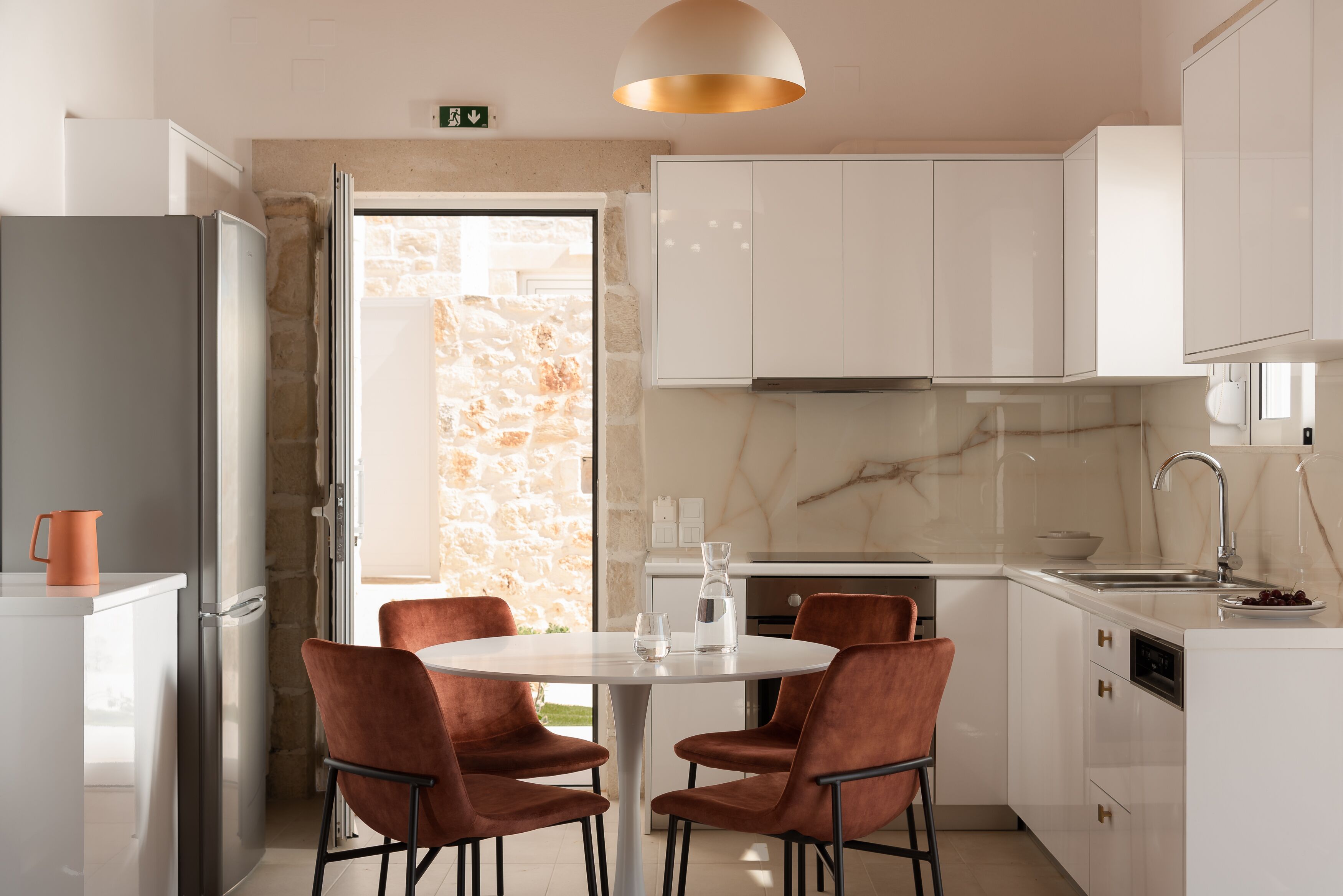 Una cocina moderna con armarios blancos, un salpicadero de mármol y una mesa redonda con cuatro sillas.
