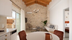 A modern kitchen with a stone wall, wooden ceiling, and a dining area with a round table and chairs. - Evaero Villa II, Family Retreat with a 32m² Pool (Prinos)
