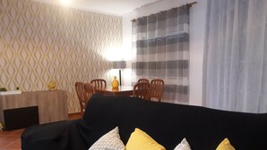 Un soggiorno con un divano nero, cuscini decorati, un tavolo da pranzo con sedie e carta da parati fantasia.