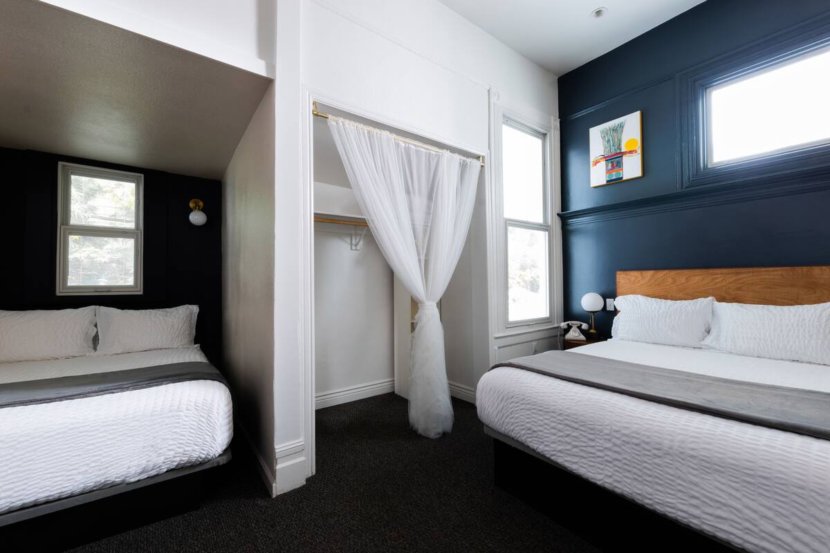A bedroom with two beds, a canopy bed, a wooden headboard, and a painting on the wall.