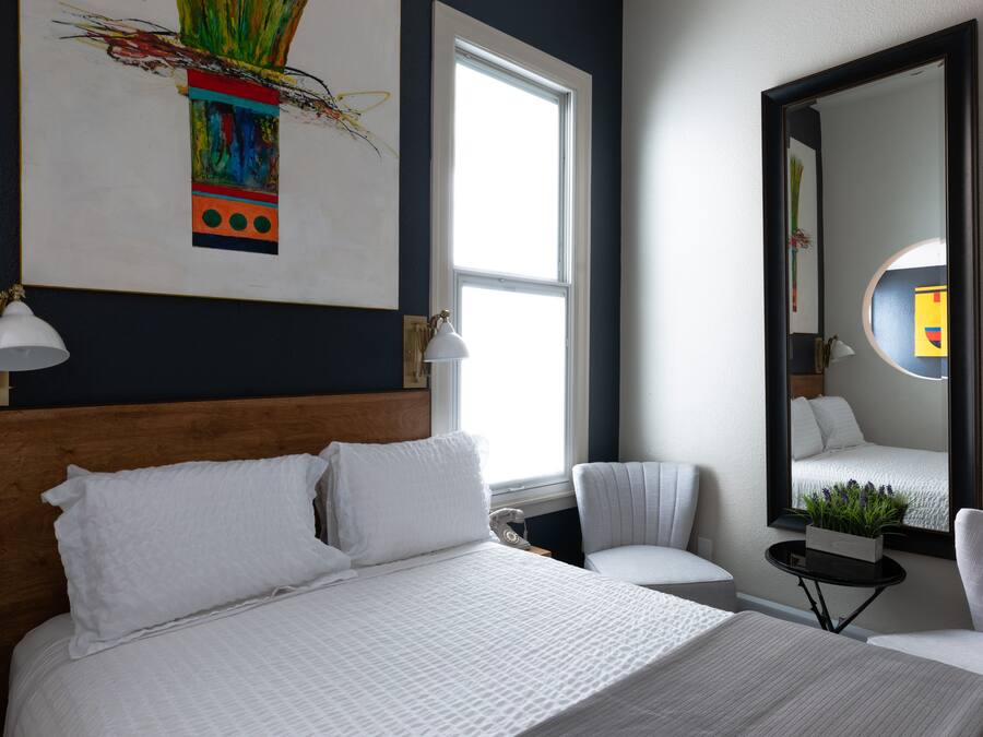 A modern hotel room with a large bed, two bedside tables, a chair, a window, and a mirror.