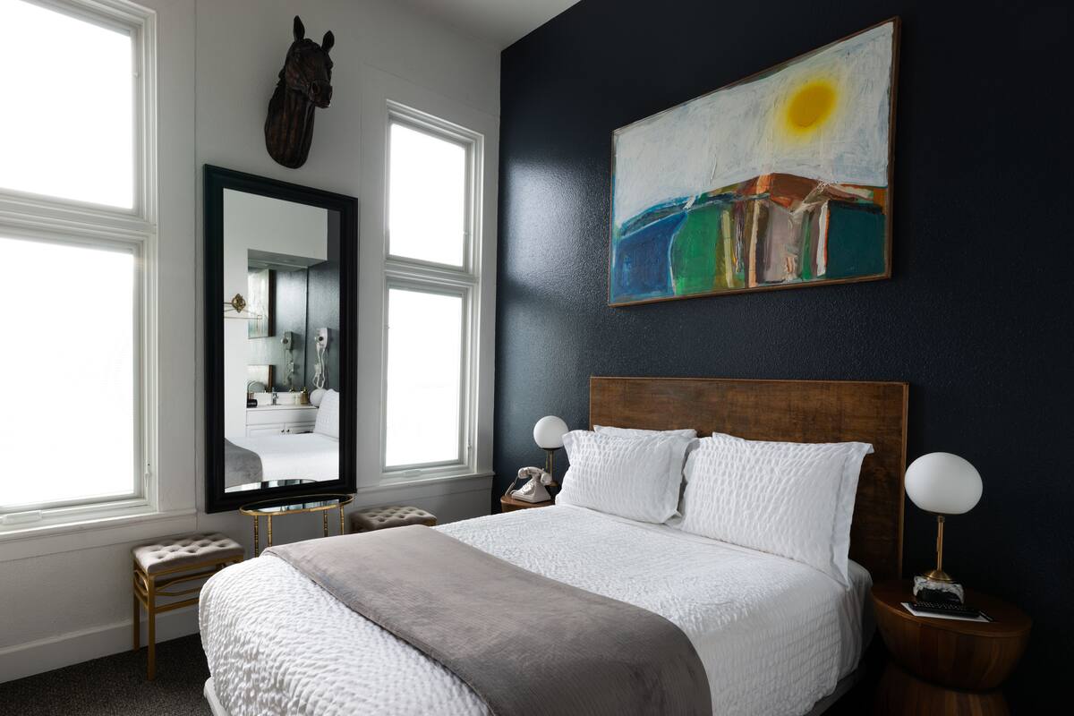 A bedroom with a large bed, a mirror, a painting, and a window.