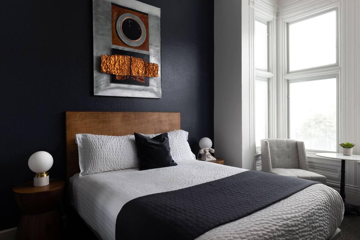 A modern bedroom with a large bed, a headboard, two bedside tables, a chair, and a window.