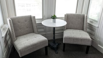 Deux fauteuils rembourrés au motif capitonné, une petite table ronde ornée d’un pot de plantes et une fenêtre avec des stores.