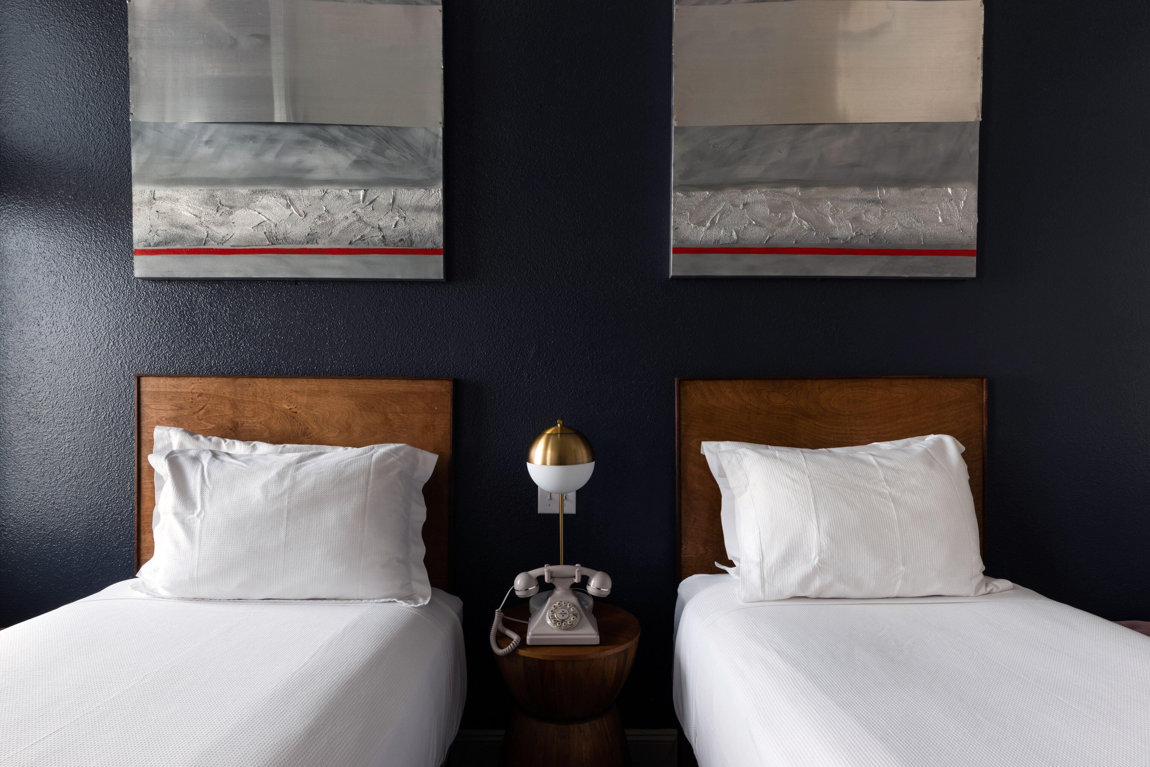 Habitación de hotel con dos camas, una mesita de noche de madera con un teléfono y una obra de arte en la pared.