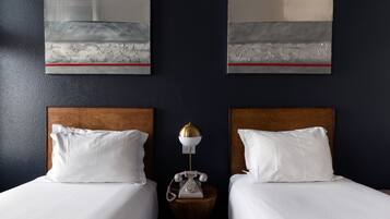 Habitación de hotel con dos camas, una mesita de noche de madera con un teléfono y una obra de arte en la pared.