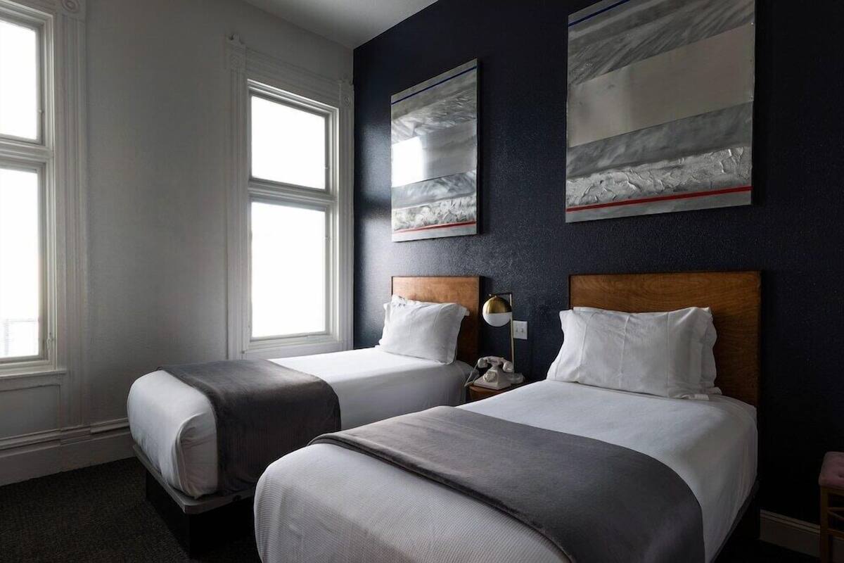 A hotel room with two beds, a window, and artwork on the wall.
