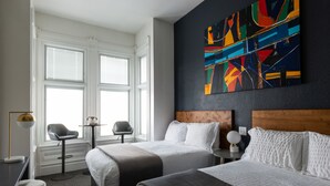A hotel room with two beds, a large abstract painting on the wall, a window with blinds, a desk with a lamp, and a chair. - The Metro Hotel (San Francisco)