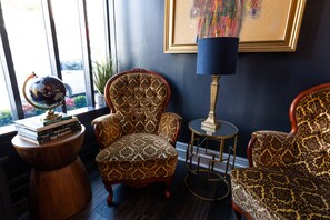 Une pièce comprenant un fauteuil à motifs, une petite table ronde avec une lampe, un globe posé sur une table d’appoint et un tableau encadré accroché au mur.