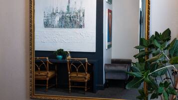 A room with a large mirror, two wicker chairs, a small table with a plant, and a dark-colored sofa.