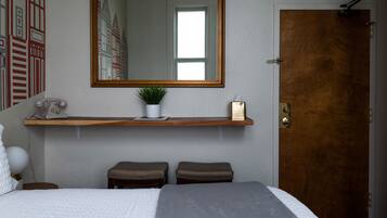 A bedroom with a large bed, a wooden door, a mirror, a shelf with a plant, and a telephone.