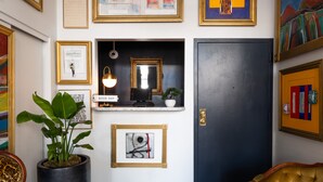 A room with a dark door, a potted plant, framed artwork, and a small shelf with a lamp. - The Metro Hotel (San Francisco)