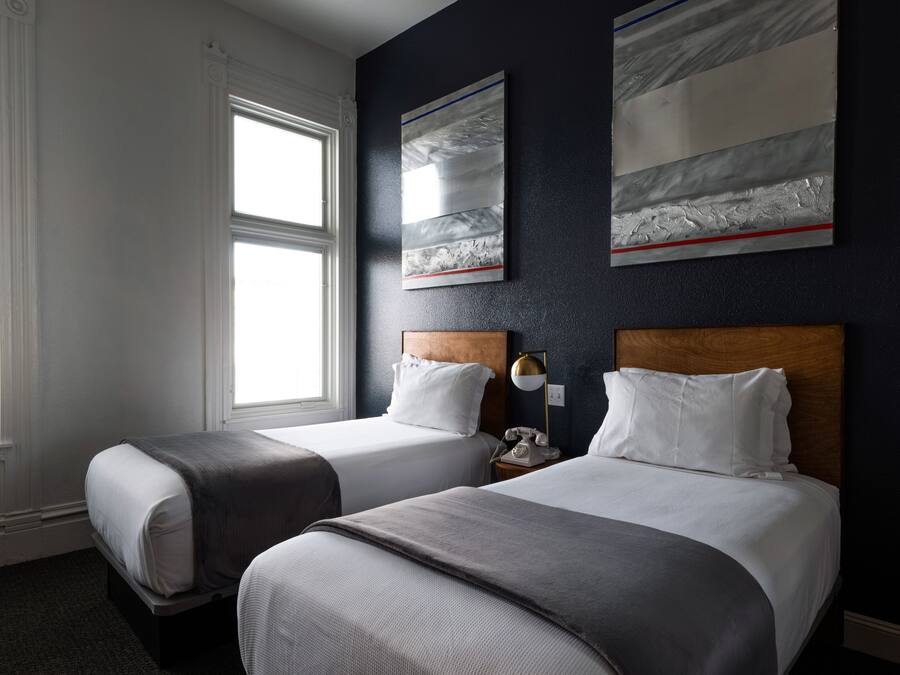 A hotel room with two beds, a wooden headboard, a nightstand with a lamp, and artwork on the wall.