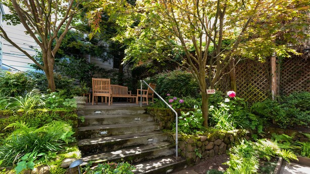 A set of stone steps leading up to a wooden bench, surrounded by lush greenery and a lattice fence. - The Metro Hotel (San Francisco)