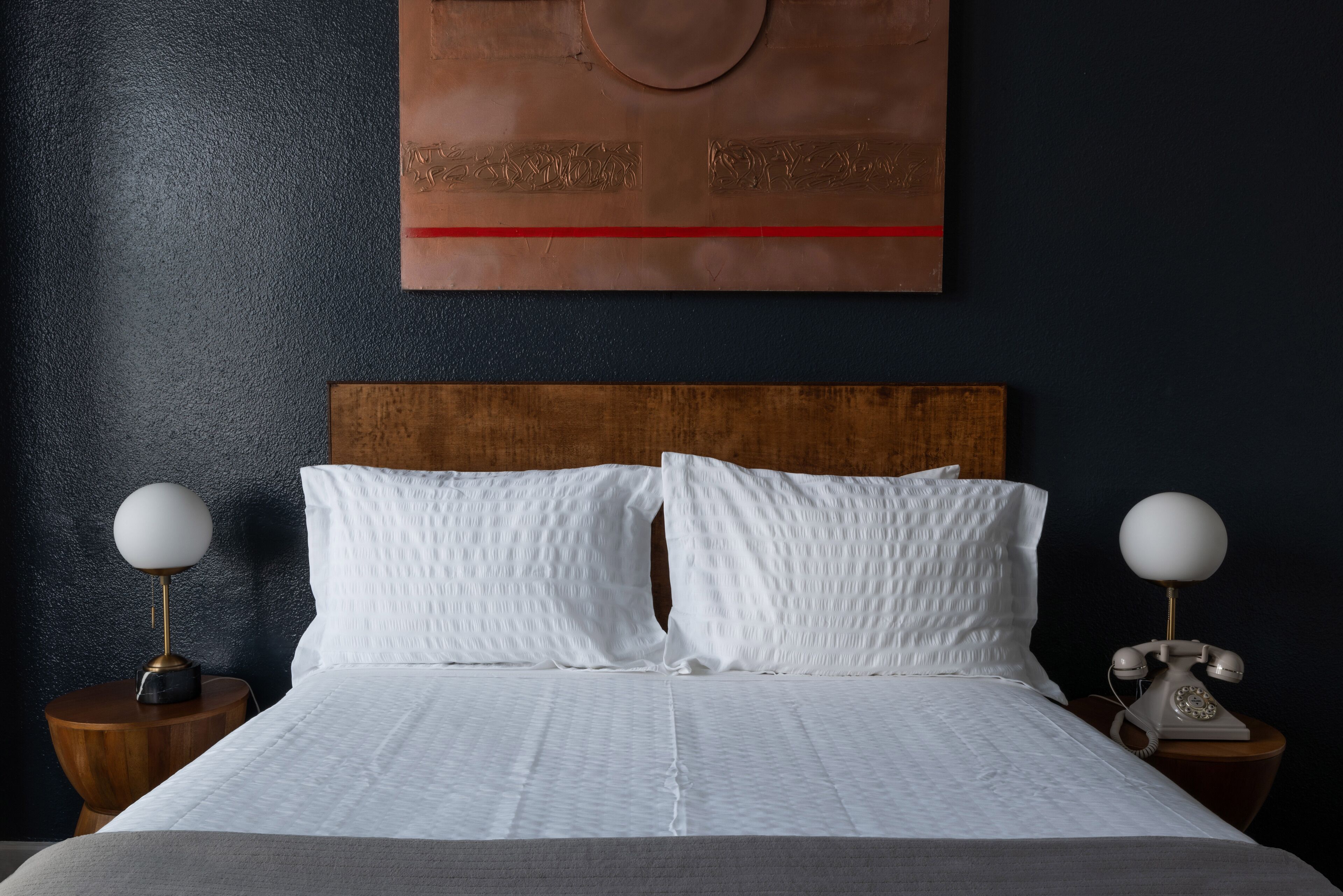 A neatly made bed with white bedding, two bedside tables with lamps, and a wall art piece above the bed.