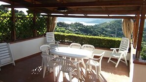 Een overdekt terras met een tafel en stoelen, met uitzicht op een weelderig groen landschap.