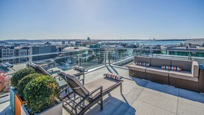 Une terrasse sur le toit dotée d’une balustrade en verre, de chaises longues, d’un canapé et offrant une vue sur le paysage urbain.