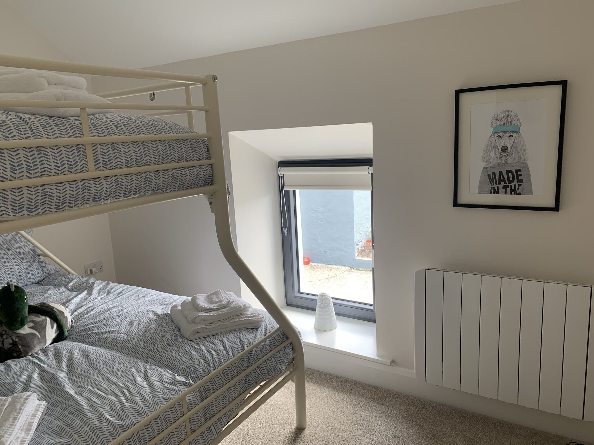 Ein Stockbett mit gemusterten Bettwäsche, ein Heizkörper, ein gerahmtes Bild an der Wand und ein Fenster mit Blick.