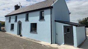 A two-story house with a light blue exterior, a dark roof, and a chimney. - Farm House - Sleeps 7 - Garden - Parking (Kinsale)