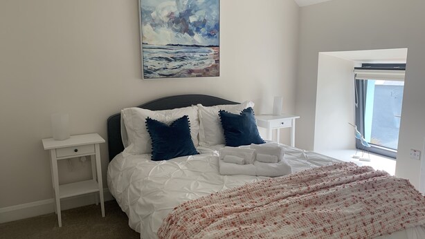 A bedroom with a bed, white nightstands, a painting, and a window with a view. - Farm House - Sleeps 7 - Garden - Parking (Kinsale)