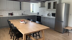 A modern kitchen with grey cabinets, a wooden dining table, and a stainless steel refrigerator. - Farm House - Sleeps 7 - Garden - Parking (Kinsale)