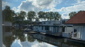 A canal with floating houses, a clear sky, and trees in the background. - Houseboat with private studio near downtown and Rai in the middle of urban greenery (Amsterdam)