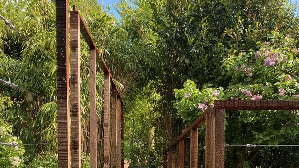 A covered walkway with a metal grid floor, surrounded by lush greenery and flowering plants. - Houseboat with private studio near downtown and Rai in the middle of urban greenery (Amsterdam)