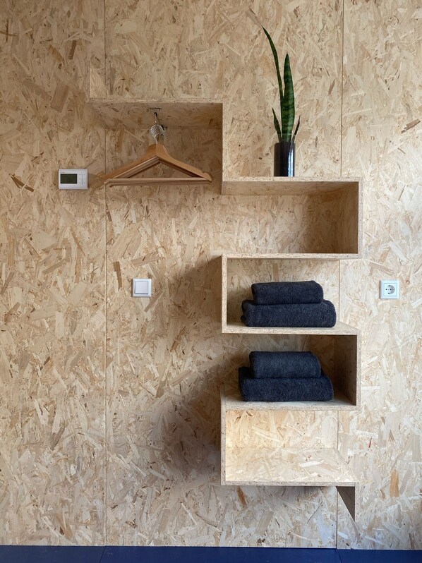 A room with a wooden wall, a thermostat, a plant, and shelves with folded towels. - Houseboat with a private studio near downtown and the Rai, surrounded by urban greenery (Amsterdam)