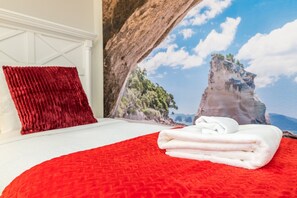 A bed with a red quilt and white towels, a red pillow, and a wall mural of a coastal landscape. - Grand 8BD Villa With Themed Rooms and Game Room! Close to Disney! #8ws883 (Kissimmee)