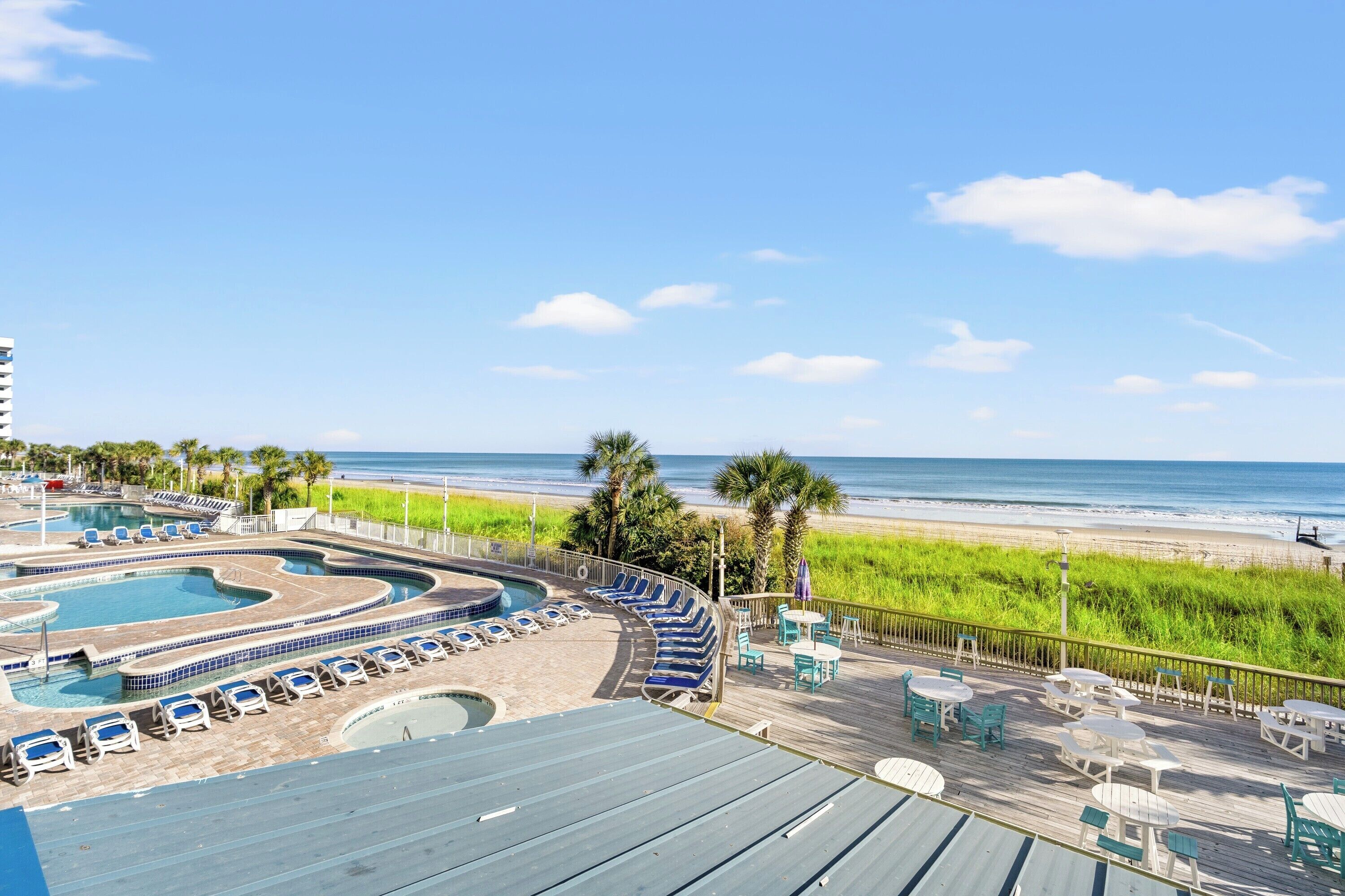 Un resort con zona de piscina, sillas de descanso y vista a la playa.