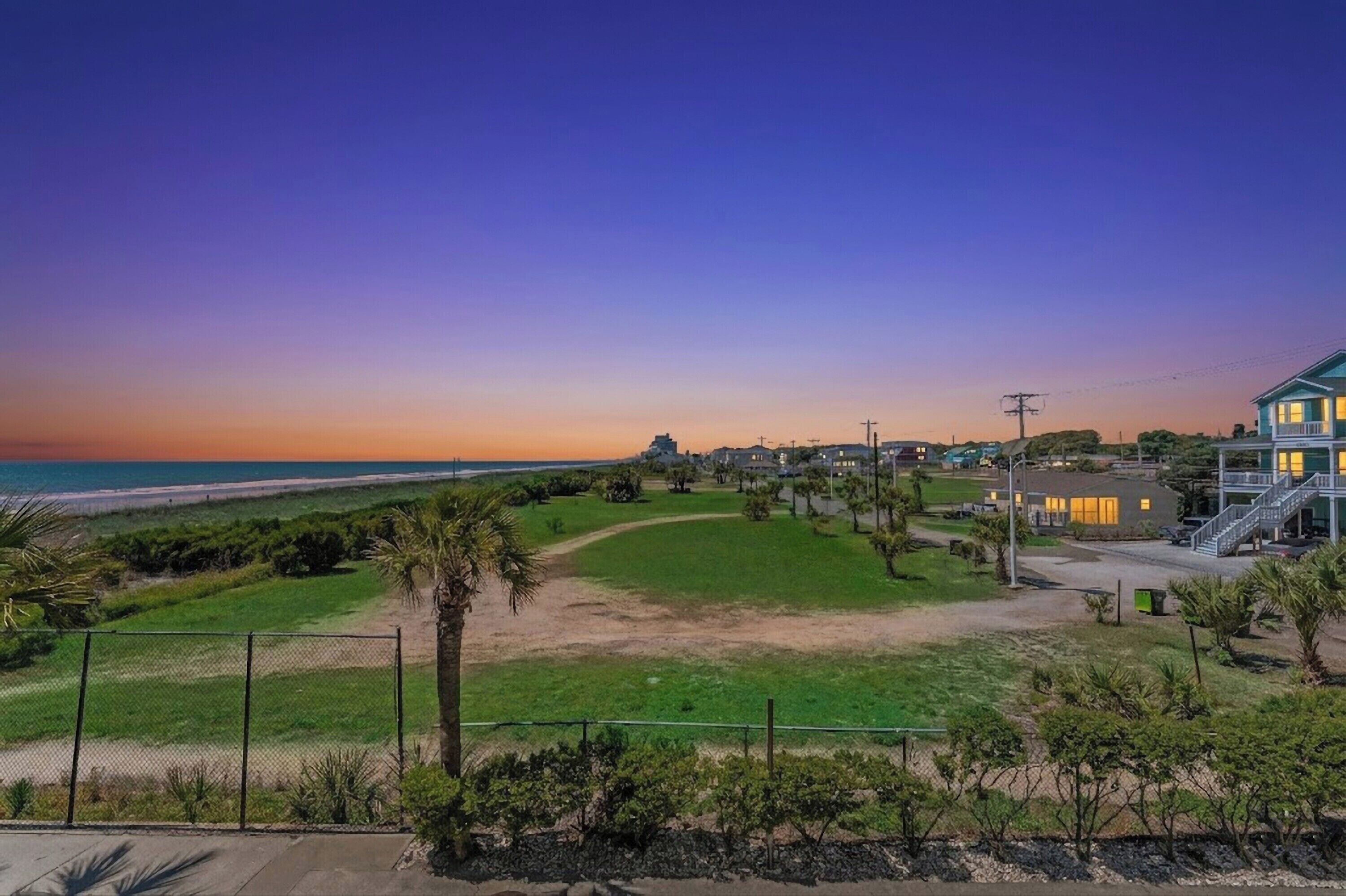 A coastal property with a view of the ocean, a fenced lawn, and a building with a staircase.