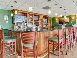 Un espace bar doté de comptoirs en bois, de chaises rembourrées de couleur verte et d’un éclairage suspendu.