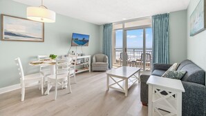Un vaste salon avec balcon, un coin repas et un espace détente comprenant un canapé et des fauteuils.