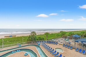 A pool area with lounge chairs and a view of the beach.