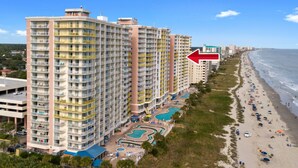 Un hotel de gran altura con varios balcones, una zona de piscina y vista al mar.